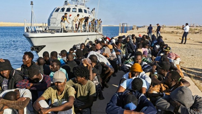 (Arquivo) Dezenas de migrantes resgatados do Mar Mediterrâneo permanecem sentados em um píer próximo a navio da guarda costeira da Líbia, em Khoms