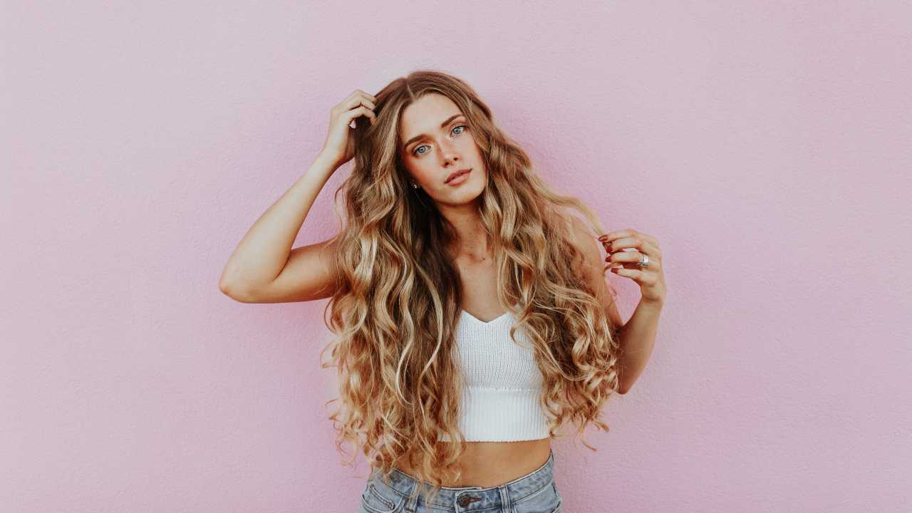 mulher loira com cabelos longos encaracolados em fundo rosa/como fazer os cabelos crescerem mais rápido