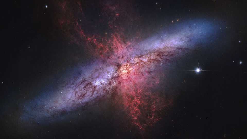 Por que a Galáxia do Charuto está soltando fumaça vermelha? M82, como é conhecida, foi despertada por uma passagem recente perto da grande galáxia espiral M81. No entanto, isso não explica totalmente a fonte do gás e da poeira em expansão externa de brilho vermelho. Evidências indicam que esse gás e poeira estão sendo expulsos pelos ventos de partículas emergentes combinados de muitas estrelas, criando um supervento galáctico. Acredita-se que as partículas de poeira se originam no meio interestelar de M82 e são realmente semelhantes em tamanho às partículas da “fumaça” do charuto. Localizada a 12 milhões de anos-luz da Terra, é a Galáxia do Charuto é a mais brilhante no céu em luz infravermelha e pode ser vista com um pequeno telescópio apontado para a direção da Constelação da Ursa Maior
