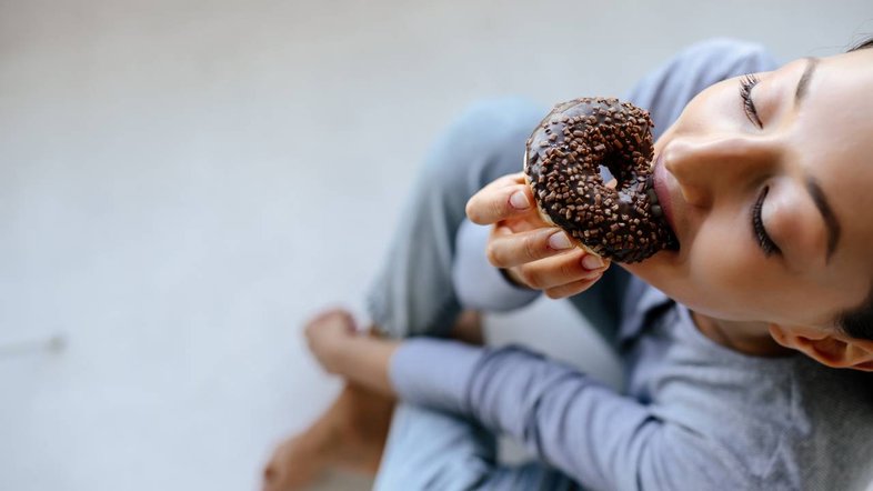 mulher comendo donut, erros alimentares que atrapalham o emagrecimento