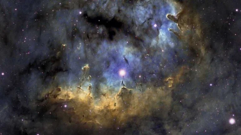 Estrelas quentes e jovens e pilares cósmicos de gás e poeira parecem se aglomerar na NGC 7822. Na borda de uma nuvem molecular gigante em direção à constelação norte de Cepheus, a brilhante região de formação de estrelas fica a cerca de 3.000 anos-luz de distância. Dentro da nebulosa, bordas brilhantes e formas escuras são destacadas nesta colorida paisagem celeste. A emissão atômica é alimentada pela radiação energética das estrelas quentes, cujos poderosos ventos e radiação também esculpem e corroem as formas mais densas dos pilares