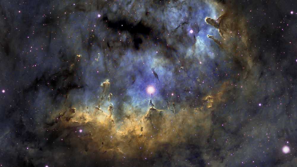 Estrelas quentes e jovens e pilares cósmicos de gás e poeira parecem se aglomerar na NGC 7822. Na borda de uma nuvem molecular gigante em direção à constelação norte de Cepheus, a brilhante região de formação de estrelas fica a cerca de 3.000 anos-luz de distância. Dentro da nebulosa, bordas brilhantes e formas escuras são destacadas nesta colorida paisagem celeste. A emissão atômica é alimentada pela radiação energética das estrelas quentes, cujos poderosos ventos e radiação também esculpem e corroem as formas mais densas dos pilares