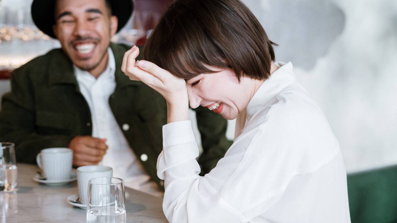 homem e mulher sentados rindo, como conhecer pessoas fora dos aplicativos de relacionamento