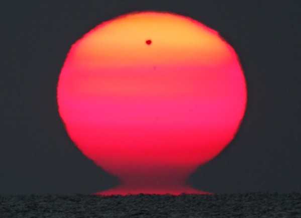 Esta imagem dramática, feita a partir do Mar Negro, mostra a silhueta de Vênus ‘nascendo’ com o Sol, um disco avermelhado e irregular. O raro trânsito de Vênus não influenciou essa forma estranha e distorcida do Sol. Ver o astro-rei na forma de um vaso etrusco é relativamente comum, especialmente se comparado aos trânsitos de Vênus. Ao pôr e ao nascer do Sol, os efeitos da refração atmosférica realçados por linhas de visão longas e baixas e fortes gradientes de temperatura atmosférica produzem distorções visuais e miragens. Essa situação é favorecida por um horizonte de mar