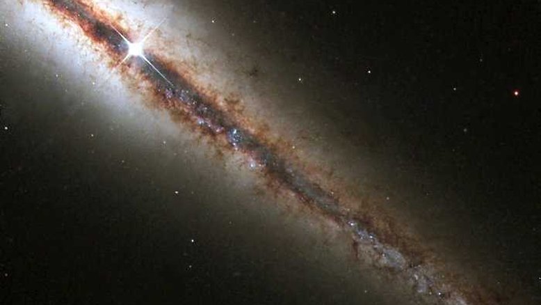O Hubble capturou NGC 4013, essa galáxia perfeitamente 'de ponta'. A nova imagem revela com detalhes enormes nuvens de poeira e gás que se estendem ao longo e acima do disco principal da galáxia. NGC 4013 é espiral, semelhante à nossa Via Láctea, situada a cerca de 55 milhões de anos-luz da Terra, na direção da Constelação de Ursa Maior. Vista de frente, pareceria um cata-vento quase circular, mas NGC 4013 ela aparece de perfil do nosso ponto de vista. Mesmo a 55 milhões de anos-luz, a galáxia é maior que o campo de visão do Hubble, e a imagem mostra apenas um pouco mais da metade do objeto