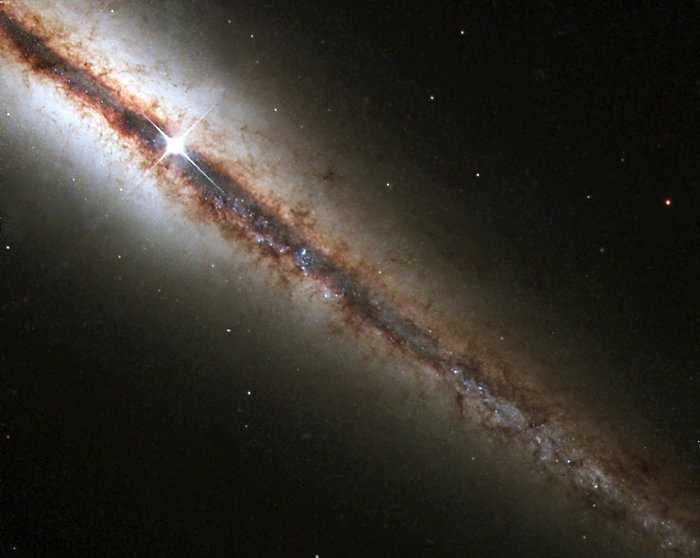O Hubble capturou NGC 4013, essa galáxia perfeitamente 'de ponta'. A nova imagem revela com detalhes enormes nuvens de poeira e gás que se estendem ao longo e acima do disco principal da galáxia. NGC 4013 é espiral, semelhante à nossa Via Láctea, situada a cerca de 55 milhões de anos-luz da Terra, na direção da Constelação de Ursa Maior. Vista de frente, pareceria um cata-vento quase circular, mas NGC 4013 ela aparece de perfil do nosso ponto de vista. Mesmo a 55 milhões de anos-luz, a galáxia é maior que o campo de visão do Hubble, e a imagem mostra apenas um pouco mais da metade do objeto