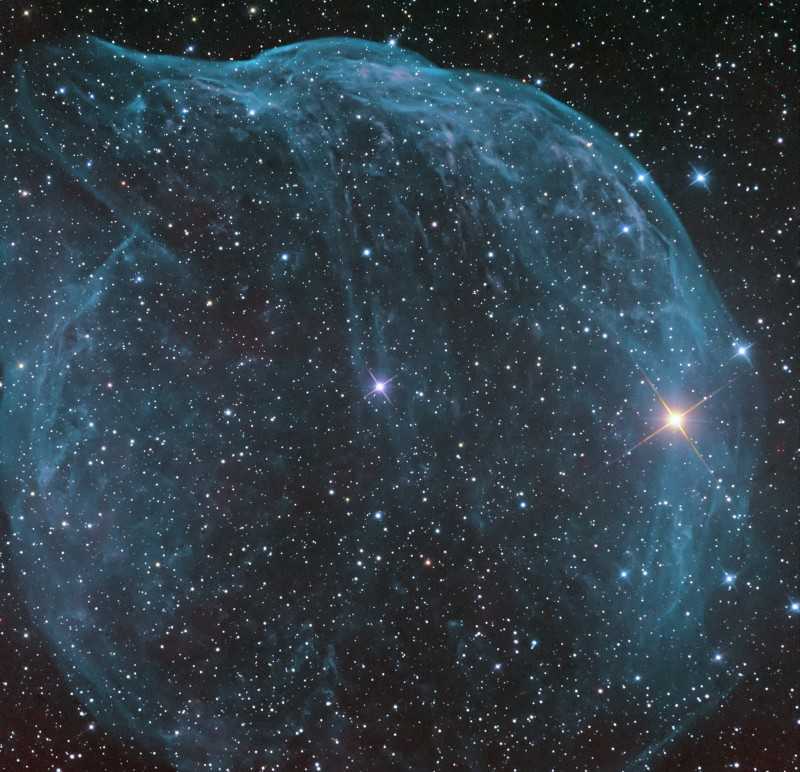 Soprada por ventos rápidos de uma estrela quente e massiva, essa bolha cósmica é enorme. Catalogada como Sharpless 308, ela fica a cerca de 5.200 anos-luz de distância, na Constelação do Cão Maior. A nebulosa soprada pelo vento tem uma idade de cerca de 70.000 anos. A emissão relativamente fraca, capturada nesta imagem, é dominada pelo brilho dos átomos de oxigênio ionizado mapeados em tons azulados