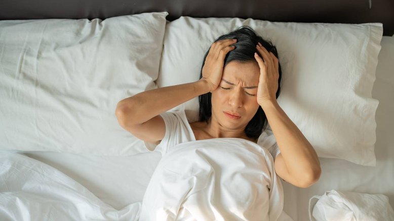 mulher deitada com as mãos na cabeça e rosto bravo, noite sem sono, noite ruim de sono