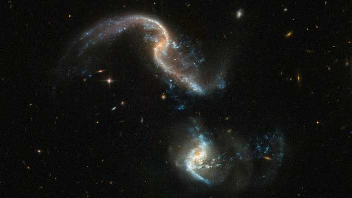Arp 256 é um sistema de duas galáxias espirais, localizado na direção da Constelação de Cetus, a cerca de 350 milhões de anos-luz de distância da Terra. Elas estão em um estágio inicial de fusão. Esta imagem, feita com o Telescópio Espacial Hubble da Nasa/ESA, mostra as duas galáxias com formas fortemente distorcidas e um número surpreendente de nós azuis. Esses pontos de formação estelar, que mais parecem fogos de artifício explodindo, foram desencadeados pela interação entre as duas galáxias