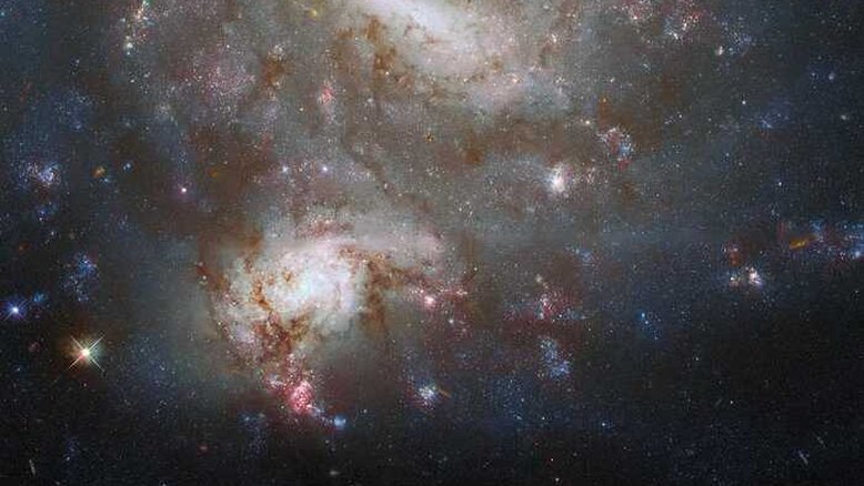 As galáxias gêmeas NGC 4496A e NGC 4496B, apesar de aparecerem lado a lado nesta imagem, estão a distâncias muito diferentes. Ambas na Constelação de Virgem, NGC 4496A está a 47 milhões de anos-luz da Terra, enquanto NGC 4496B está a 212 milhões de anos-luz. A enorme distância entre as duas galáxias significa que elas não estão interagindo entre si, mas que parecem se sobrepor devido a um alinhamento casual. A poeira galáctica pode ser vista nesta imagem como tentáculos escuros. Ela absorve a luz das estrelas, fazendo com que pareçam mais escuras