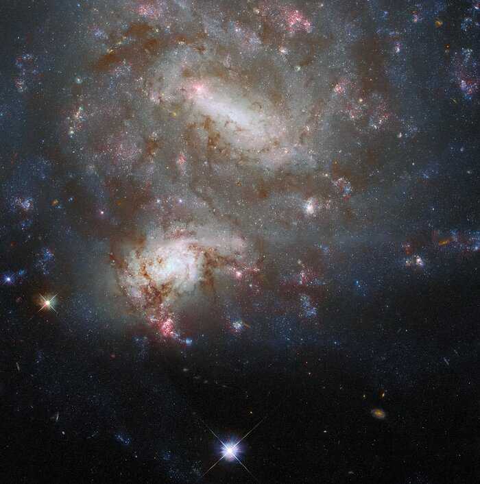 As galáxias gêmeas NGC 4496A e NGC 4496B, apesar de aparecerem lado a lado nesta imagem, estão a distâncias muito diferentes. Ambas na Constelação de Virgem, NGC 4496A está a 47 milhões de anos-luz da Terra, enquanto NGC 4496B está a 212 milhões de anos-luz. A enorme distância entre as duas galáxias significa que elas não estão interagindo entre si, mas que parecem se sobrepor devido a um alinhamento casual. A poeira galáctica pode ser vista nesta imagem como tentáculos escuros. Ela absorve a luz das estrelas, fazendo com que pareçam mais escuras