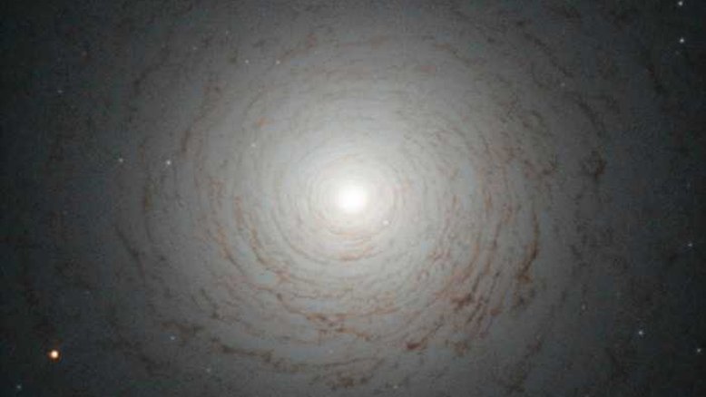 Este redemoinho cósmico é o centro da galáxia NGC 524, localizada na Constelação de Peixes, a cerca de 90 milhões de anos-luz da Terra. NGC 524 é uma galáxia lenticular, um estado intermediário na evolução galáctica, que não é elíptica e nem espiral. As espirais são galáxias de meia-idade com braços giratórios e milhões de estrelas. Junto a essas estrelas, estão grandes nuvens de gás e poeira que, quando densas o suficiente, são os berçários para novas estrelas. Quando todo o gás se esgota, os braços da galáxia desaparecem e sua forma espiral enfraquece. No final desse processo, o que resta é uma galáxia lenticular, ou seja, um disco brilhante cheio de estrelas vermelhas e velhas, cercadas por pouco gás e poeira