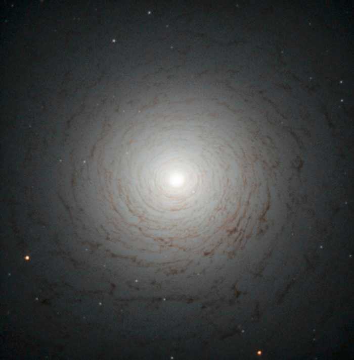 Este redemoinho cósmico é o centro da galáxia NGC 524, localizada na Constelação de Peixes, a cerca de 90 milhões de anos-luz da Terra. NGC 524 é uma galáxia lenticular, um estado intermediário na evolução galáctica, que não é elíptica e nem espiral. As espirais são galáxias de meia-idade com braços giratórios e milhões de estrelas. Junto a essas estrelas, estão grandes nuvens de gás e poeira que, quando densas o suficiente, são os berçários para novas estrelas. Quando todo o gás se esgota, os braços da galáxia desaparecem e sua forma espiral enfraquece. No final desse processo, o que resta é uma galáxia lenticular, ou seja, um disco brilhante cheio de estrelas vermelhas e velhas, cercadas por pouco gás e poeira