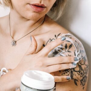 mulher com tatuagem no braço aplicando creme/cuidados pós-tatuagem