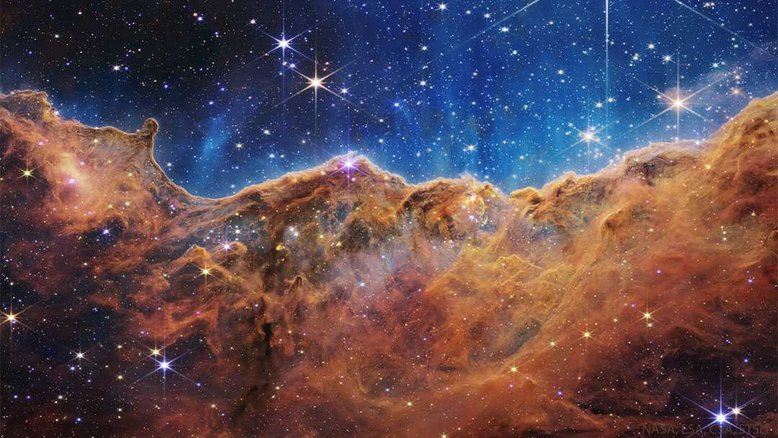 Os ventos destrutivos e a luz energética das estrelas no aglomerado aberto NGC 3324 erodiram parte de uma montanha de poeira interestelar escura, na parte norte da Nebulosa de Carina. Várias dessas estrelas estão visíveis no topo desta imagem detalhada, feita pelo tecnológico Telescópio Espacial James Webb. As falésias irregulares em destaque estão na parte de Carina conhecida como Nebulosa Gabriela Mistral, que recebeu esse nome em homenagem à famosa poeta chilena de mesmo nome, pois essas formações lembram o seu perfil facial, dependendo do ângulo de visão. Esses penhascos nebulares estão a cerca de 7,6 mil anos-luz de distância, na direção da austral Constelação de Carina