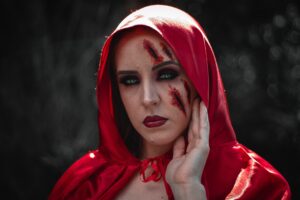 mulher com fantasia de chapéuzinho vermelho e machucado falso no rosto, maquiagem para o halloween