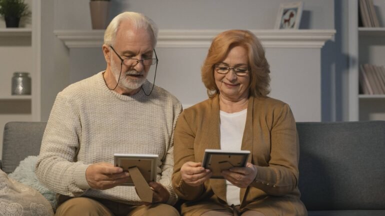 casal de idosos sentados no sofá e olhando porta-retratos
