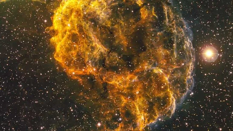 A Nebulosa da Água-Viva, também conhecida por seu nome oficial IC 443, é o remanescente de uma supernova situada a 5 mil anos-luz da Terra, na Constelação de Gêmeos. As observações mostram que a explosão que criou a Nebulosa da Água-Viva também pode ter formado um objeto peculiar, localizado na borda Sul do remanescente. Recebendo o nome de J0617, ele é provavelmente uma estrela de nêutrons girando rapidamente, ou seja, um pulsar. Pulsares se formam quando uma estrela massiva implode, formando um núcleo estelar denso, chamado de estrela de nêutrons. Uma estrela de nêutrons giratória, com um feixe de radiação, recebe o nome de pulsar