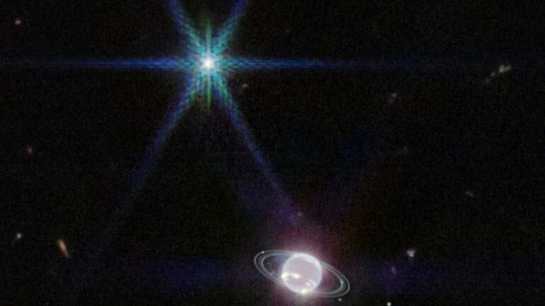 O gigante e anelado planeta gelado, Netuno, está na parte inferior desta imagem feita pelo Telescópio Espacial James Webb. Ele é o planeta do Sistema Solar mais distante do Sol, ficando cerca de 30 vezes mais longe que o planeta Terra em relação à sua estrela central. A aparência escura e fantasmagórica do planeta se deve ao metano atmosférico, que absorve a luz infravermelha. As nuvens que alcançam a maior parte do metano absorvente de Netuno se destacam na imagem. Revestido com nitrogênio congelado, Tritão - a maior lua de Netuno -, é visto no canto superior esquerdo, com os picos de difração característicos do Webb. Os anéis de Netuno também aparecem bem nítidos neste novo retrato planetário