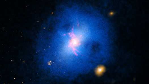 Abell 2597 é um aglomerado de galáxias a cerca de um bilhão de anos-luz da Terra, na direção da Constelação de Aquário. Ele está entre os mais de 200 objetos desse tipo que foram estudados para determinar como os buracos negros gigantes afetam o crescimento e a evolução de galáxias. Segundo o estudo, em algumas delas, o gás quente consegue arrefecer rapidamente por radiação e perda de energia. As nuvens de gás frio resultantes caem no buraco negro supermassivo central, produzindo jatos que aquecem o gás e impedem o resfriamento adicional. Esse processo, que evita que as nuvens frias fiquem muito fortes, vem ocorrendo nos últimos 7 bilhões de anos ou mais. Esta imagem composta reúne dados de raios-X (azul), luz óptica (amarelo) e emissão de átomos de hidrogênio (vermelho)