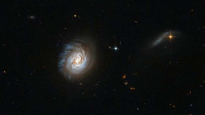 A figura dominante no meio desta imagem é a galáxia MCG-03-04-014, localizada na direção da Constelação de Cetus. Ela pertence ao grupo das galáxias infravermelhas luminosas, dado o seu alto brilho no espectro infravermelho. MCG-03-04-014 mostra faíscas brilhantes de formação estelar espalhadas por toda a galáxia, com faixas de poeira escura obscurecendo seu bulbo central brilhante. A galáxia parece mostrar evidências de perturbação: no topo dela, há fragmentos brilhantes riscando o espaço, mas o fundo é liso e arredondado. Essa aparência assimétrica significa que outro objeto está puxando a galáxia e distorcendo sua simetria