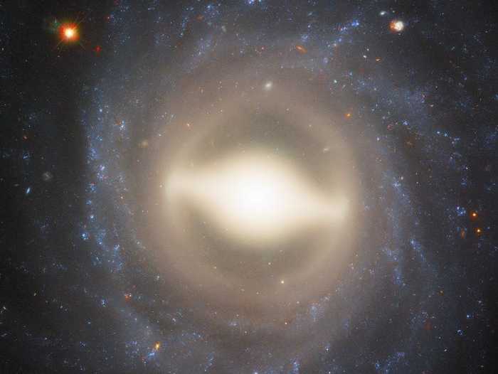 Nesta imagem, a galáxia NGC 1015, localizada na Constelação de Cetus, a 118 milhões de anos-luz da Terra aparece de frente. Dado o seu centro grande e brilhante e os braços espirais bem enrolados, como uma espécie de “barra” central de gás e estrelas, NGC 1015 foi classificada como uma galáxia espiral barrada, assim como a nossa Via Láctea. As barras são encontradas em cerca de dois terços de todas as galáxias espirais. Acredita-se que os buracos negros no centro das espirais barradas canalizam gás e energia dos braços externos para o núcleo através dessas barras brilhantes, alimentando o nascimento de estrelas no centro. Em 2009, uma supernova foi detectada em NGC 1015 e aparece em um dos pontos brilhantes no canto superior direito do centro da galáxia