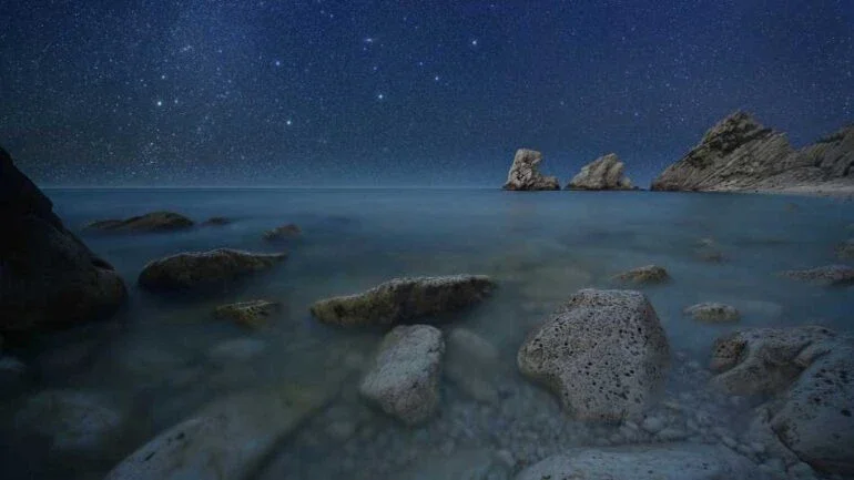 A Galáxia de Andrômeda, a 2,5 milhões de anos-luz de distância, é o objeto mais distante visível a olho a partir da Terra. Outros objetos aparentes no céu noturno, como estrelas, aglomerados e nebulosas, estão entre centenas e milhares de anos-luz de distância, localizados dentro da nossa Via Láctea. Também conhecida como M31, a Galáxia de Andrômeda é a mancha tênue, perto do centro superior desta paisagem celeste, captada na região de Monte Conero, na costa do Mar Adriático, na Itália. Como as estrelas se arrastavam acima do horizonte enquanto a foto era feita, exposições separadas foram combinadas para retratar esta cena sublime