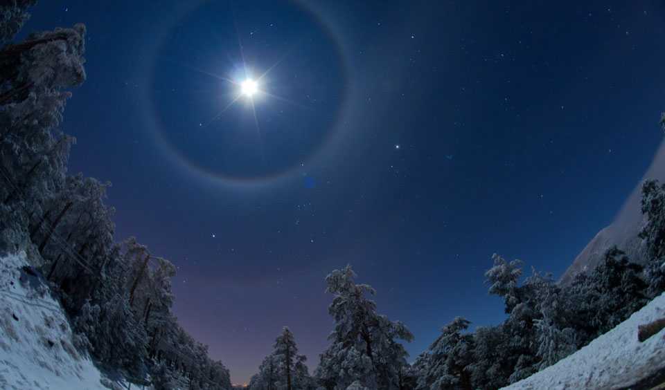 Cristais de gelo na atmosfera atuam como uma lente gigante, fazendo com que arcos e halos apareçam ao redor do Sol ou da Lua. Nesta imagem, feita em janeiro de 2012, perto de Madri, na Espanha, a Lua está acompanhada de quatro halos lunares, sendo o objeto mais brilhante no céu. O satélite natural da Terra estar adornado por um halo quádruplo é algo extremamente difícil de acontecer. Ao fundo, está Sirius, a principal estrela da Constelação do Cão Maior, as estrelas do cinturão de Orion e Betelgeuse, que também pertence à Constelação de Orion. Halos e arcos geralmente duram de minutos a horas, em um fenômeno incomum e de rara beleza