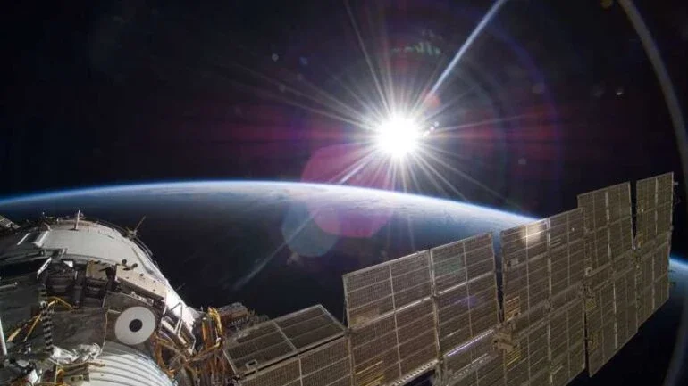 Eis uma imagem de tirar o fôlego, feita diretamente da Estação Espacial Internacional (ISS), em novembro de 2009. O Sol, a superfície terrestre e o longo braço de um painel solar estão visíveis neste registro feito quando o ônibus espacial Atlantis visitou o empreendimento científico e tecnológico que está em órbita da Terra. Os reflexos da janela e da lente hexagonal da câmera estão sobrepostos. O ônibus espacial Atlantis foi uma das missões bem-sucedidas com o objetivo de expandir e reabastecer a ISS. Resultado de uma iniciativa colaborativa entre diversos países, a ISS tem realizado inúmeros estudos científicos no ambiente de microgravidade no qual opera, além de servir como observatório terrestre