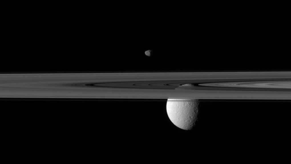 Nesta imagem, destacam-se duas luas de Saturno e seus anéis. Reia, a maior delas, está parcialmente escondida atrás de alguns dos anéis de Saturno, neste registro feito, em 2010, pela espaçonave robótica Cassini. Embora pareça estar pairando sobre os anéis, a pequena Janus está bem atrás deles. Janus é uma das luas menores de Saturno e mede apenas cerca de 180 quilômetros de diâmetro. Por sua vez, Reia é muito maior, medindo 1,5 mil quilômetros de diâmetro. O topo de Reia é visível apenas através de lacunas nos anéis. Depois de uma década de muitas descobertas, a espaçonave Cassini ficou sem combustível, em 2017, sendo direcionada para entrar na atmosfera de Saturno, onde certamente derreteu