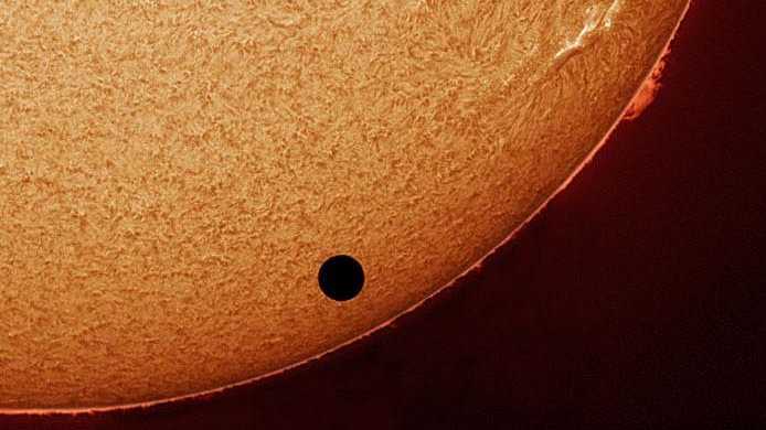 Durante o trânsito de Vênus, em 2004, o astrônomo Stefan Seip registrou esta detalhada imagem do Sol, a partir de Stuttgart, na Alemanha. A foto telescópica foi feita com um filtro H-alfa, que transmite apenas a luz vermelha dos átomos de hidrogênio e enfatiza a cromosfera solar, ou seja, a região da atmosfera do Sol imediatamente acima de sua fotosfera ou superfície visível. Embora o disco escuro de Vênus pareça estar imitando uma mancha solar gigante na foto, trata-se, de fato, da imagem de nosso vizinho no Sistema Solar
