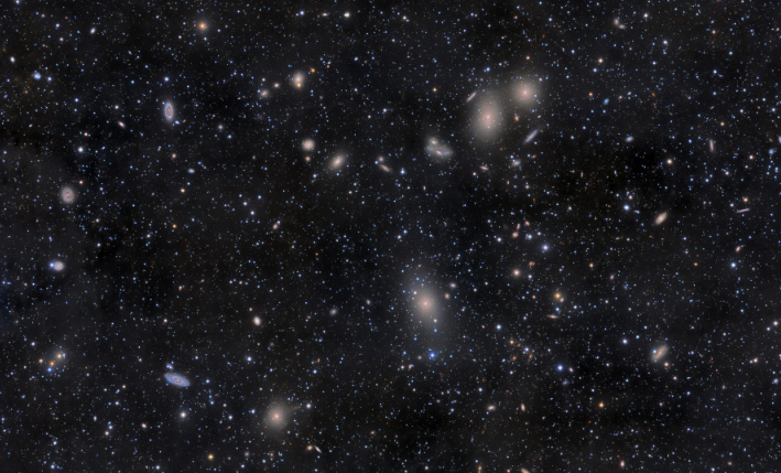 Bem mais de mil galáxias são membros conhecidos do Aglomerado de Virgem, o grande aglomerado de galáxias mais próximo do nosso próprio Grupo Local. Este mosaico de imagens telescópicas registra a região central dele através de fracas nuvens de poeira em primeiro plano que permanecem acima do plano de nossa própria galáxia, a Via Láctea. A galáxia elíptica gigante dominante do aglomerado, M87, está logo abaixo do centro do quadro. Acima de M87 está o famoso par de galáxias em interação NGC 4438. Em média, as galáxias do Aglomerado de Virgem estão a cerca de 48 milhões de anos-luz de distância, na direção da Constelação de Virgem. A distância do Aglomerado de Virgem tem sido usada para fornecer uma determinação importante da Constante de Hubble e da escala do Universo