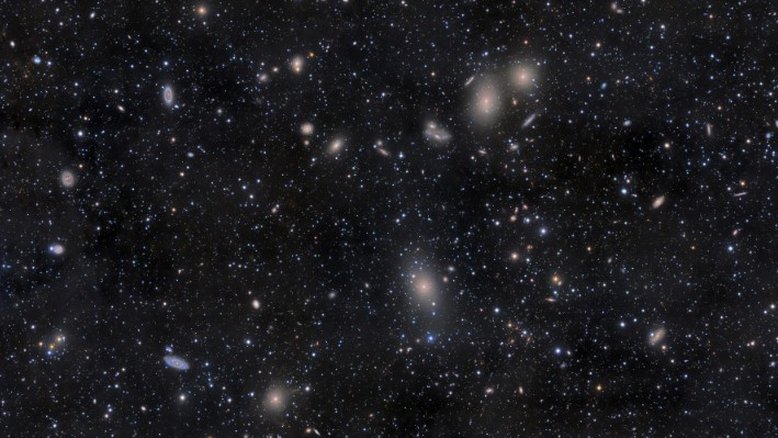 Bem mais de mil galáxias são membros conhecidos do Aglomerado de Virgem, o grande aglomerado de galáxias mais próximo do nosso próprio Grupo Local. Este mosaico de imagens telescópicas registra a região central dele através de fracas nuvens de poeira em primeiro plano que permanecem acima do plano de nossa própria galáxia, a Via Láctea. A galáxia elíptica gigante dominante do aglomerado, M87, está logo abaixo do centro do quadro. Acima de M87 está o famoso par de galáxias em interação NGC 4438. Em média, as galáxias do Aglomerado de Virgem estão a cerca de 48 milhões de anos-luz de distância, na direção da Constelação de Virgem. A distância do Aglomerado de Virgem tem sido usada para fornecer uma determinação importante da Constante de Hubble e da escala do Universo
