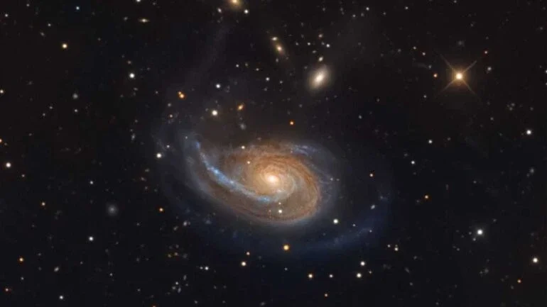 A peculiar galáxia espiral Arp 78 está dentro dos limites da Constelação de Áries, a cerca de 100 milhões de anos-luz de distância, para além das estrelas e nebulosas de nossa galáxia, a Via Láctea. Também conhecida como NGC 772, ela tem mais de 100 mil anos-luz de diâmetro e ostenta um único braço espiral externo proeminente neste retrato cósmico detalhado. Sua galáxia companheira mais brilhante, a compacta NGC 770, está no canto superior direito. A aparência difusa e elíptica de NGC 770 contrasta com uma estrela da Via Láctea, que aparece brilhando em primeiro plano, em tom amarelado