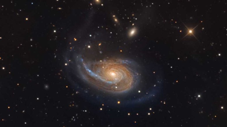A peculiar galáxia espiral Arp 78 está dentro dos limites da Constelação de Áries, a cerca de 100 milhões de anos-luz de distância, para além das estrelas e nebulosas de nossa galáxia, a Via Láctea. Também conhecida como NGC 772, ela tem mais de 100 mil anos-luz de diâmetro e ostenta um único braço espiral externo proeminente neste retrato cósmico detalhado. Sua galáxia companheira mais brilhante, a compacta NGC 770, está no canto superior direito. A aparência difusa e elíptica de NGC 770 contrasta com uma estrela da Via Láctea, que aparece brilhando em primeiro plano, em tom amarelado