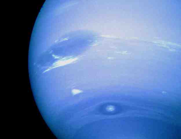 Netuno tem manchas. O gigante gasoso mais externo do Sistema Solar mostra uma tonalidade azul quase uniforme, criada por pequenas quantidades de metano, flutuando em uma espessa atmosfera de hidrogênio e hélio, quase incolores. As manchas escuras que aparecem são anticiclones: grandes sistemas de alta pressão que giram no topo de suas nuvens frias. Duas manchas escuras são visíveis nesta imagem feita pela espaçonave Voyager 2, em 1989. Imagens posteriores de Netuno, feitas pelo Telescópio Espacial Hubble, em 1994, indicaram que ambas as manchas escuras haviam se dissipado e outra havia sido criada