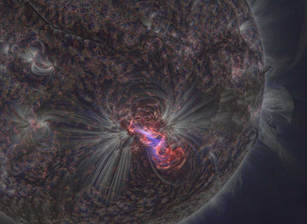 A região solar AR2192 é uma das mais ativas e abrangentes do Sol. Esta imagem, feita em 2014, registra uma de suas diversas explosões altamente energéticas. A cena é uma combinação de cores de imagens feitas em três diferentes comprimentos de onda de luz ultravioleta extrema. A emissão, de átomos de ferro e hélio altamente ionizados, traça linhas de campo magnético que percorrem o plasma quente da cromosfera externa e da coroa do Sol. Abaixo, a fotosfera solar mais fria parece escura