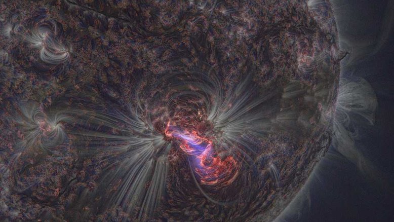 A região solar AR2192 é uma das mais ativas e abrangentes do Sol. Esta imagem, feita em 2014, registra uma de suas diversas explosões altamente energéticas. A cena é uma combinação de cores de imagens feitas em três diferentes comprimentos de onda de luz ultravioleta extrema. A emissão, de átomos de ferro e hélio altamente ionizados, traça linhas de campo magnético que percorrem o plasma quente da cromosfera externa e da coroa do Sol. Abaixo, a fotosfera solar mais fria parece escura