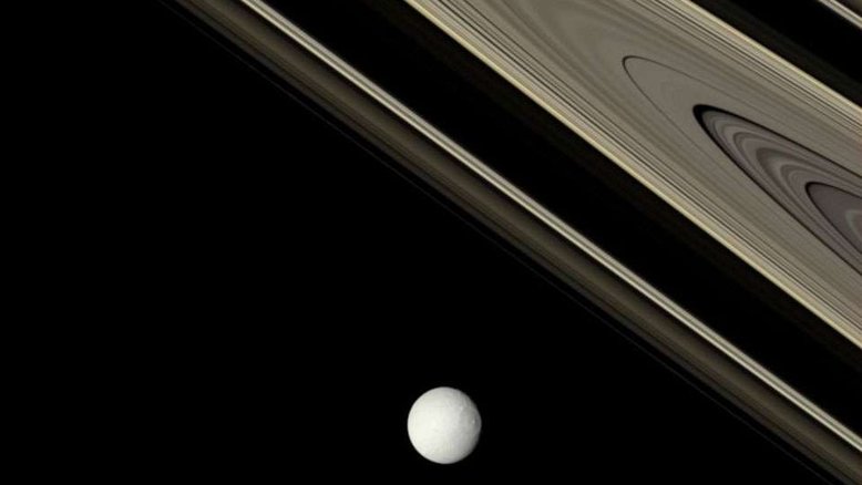 Qual a idade dos anéis de Saturno? Ninguém sabe ao certo. Talvez eles tenham sido formados há relativamente pouco tempo na história do Sistema Solar, apenas há cerca de 100 milhões de anos, quando um objeto do tamanho de uma lua foi partido perto do planeta. Evidências mais recentes, no entanto, levantam a possibilidade de que alguns dos anéis de Saturno possam ter bilhões de anos, sendo tão antigos quanto o próprio planeta. Nesta imagem, os anéis do gigante gasoso foram fotografados em suas cores reais pela espaçonave Cassini. A brilhante e gelada Tétis, uma das luas de Saturno, iluminada por uma chuva de gelo da lua irmã Encélado, é destacada em primeiro plano