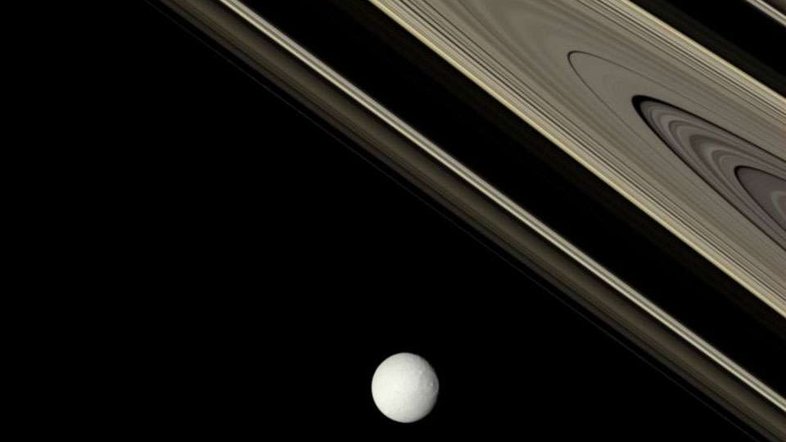 Qual a idade dos anéis de Saturno? Ninguém sabe ao certo. Talvez eles tenham sido formados há relativamente pouco tempo na história do Sistema Solar, apenas há cerca de 100 milhões de anos, quando um objeto do tamanho de uma lua foi partido perto do planeta. Evidências mais recentes, no entanto, levantam a possibilidade de que alguns dos anéis de Saturno possam ter bilhões de anos, sendo tão antigos quanto o próprio planeta. Nesta imagem, os anéis do gigante gasoso foram fotografados em suas cores reais pela espaçonave Cassini. A brilhante e gelada Tétis, uma das luas de Saturno, iluminada por uma chuva de gelo da lua irmã Encélado, é destacada em primeiro plano