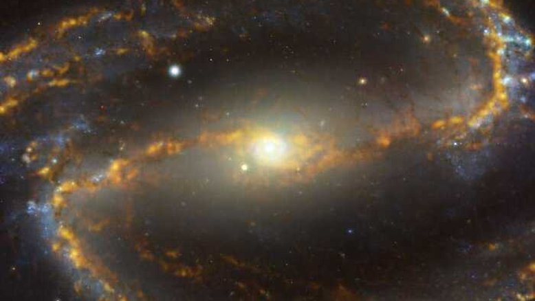 A galáxia NGC 1300 está localizada a aproximadamente 61 milhões de anos-luz da Terra, na Constelação de Eridanus. Ela é uma galáxia espiral, com uma barra de estrelas e gás –– visto aqui cruzando a imagem horizontalmente –– e um anel central de intensa formação estelar. Esta imagem é uma combinação de observações realizadas em diferentes cores –– ou comprimentos de onda –– de luz. O tom caramelo e com brilho dourado corresponde a nuvens de gás molecular, a matéria-prima a partir da qual as estrelas se formam. As regiões azuladas, ao fundo, revelam a distribuição de estrelas mais velhas e já formadas