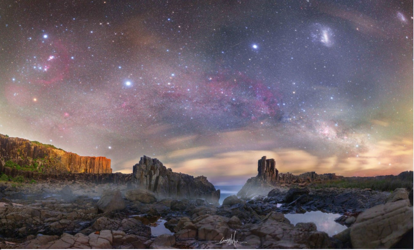 Eis uma paisagem celeste cheia de ícones e estrelas famosas. Na extrema esquerda está a Constelação de Órion, com as icônicas três estrelas alinhadas em seu cinturão e a famosa Nebulosa de Órion. Logo à esquerda do centro da imagem está a estrela mais brilhante da noite: Sirius, a principal da Constelação do Cão Maior. Na extrema direita, perto do topo, estão duas galáxias satélites da Via Láctea: a Grande Nuvem de Magalhães e a Pequena Nuvem de Magalhães. Também na extrema direita, logo acima do horizonte, está a Constelação do Cruzeiro do Sul. Este registro foi feito na Austrália, nos últimos dias de 2021
