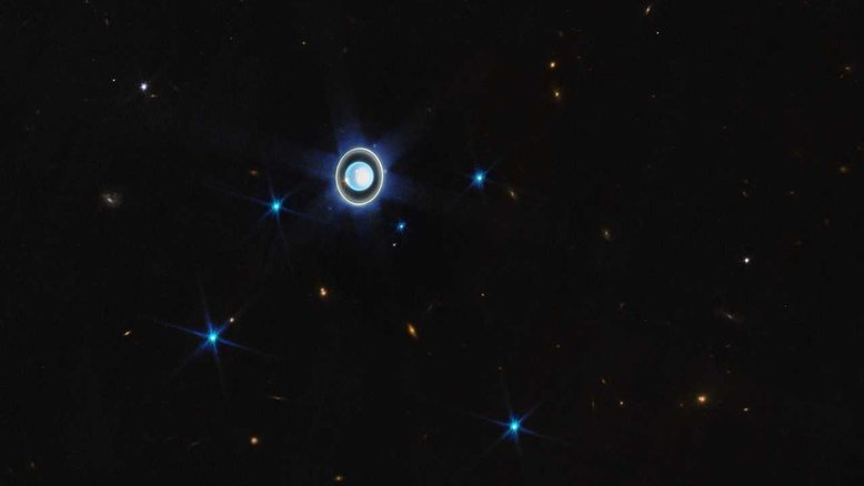 Esta visão ampla, registrada pelo Telescópio Espacial James Webb, mostra o planeta Urano rodeado por seis de suas 27 luas conhecidas. Vistas aqui como pequenos pontos azuis e brilhantes, estão Ariel, Puck, Miranda, Umbriel, Titânia e Oberon. Os seus demais satélites naturais são muito pequenos e fracos para que fossem notados nesta exposição de curta duração. Os pontos mais amarelados da imagem representam variados objetos de fundo, incluindo galáxias vizinhas à Via Láctea