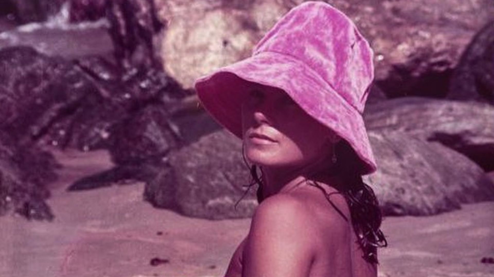 foto antiga de vera fischer nua, de costas, em uma praia. ela veste apenas um chapéu.
