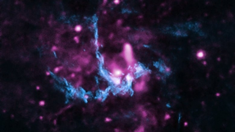Esta imagem composta, feita em 2013, apresenta dados de raios X (roxo) e de rádio (azul) da região de Sagittarius A* (ou Sgr A*), o buraco negro supermassivo que habita o centro da Via Láctea, a nossa galáxia. Sgr A* tem aproximadamente 4 milhões de vezes a massa do Sol e fica a cerca de 26 mil anos-luz da Terra, na direção da Constelação de Sagitário. Com esse registro, foi possível avaliar a presença de um jato de partículas de alta energia, saindo do buraco negro para viajar pelo espaço até atingir o gás a vários anos-luz de distância. Essa região central da Via Láctea tem muitos aglomerados de gás e poeira e a interação desse material com os jatos de partículas desencadeia a formação de uma frente de choque
