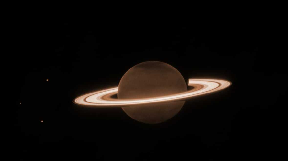 No final do mês passado, o Telescópio Espacial James Webb fez as primeiras observações de Saturno, em comprimentos de onda próximos ao infravermelho. O planeta parece escurecido nesse espectro, pois o gás metano absorve quase toda a luz solar que incide na atmosfera. No entanto, os anéis permanecem brilhantes. Três de suas luas estão visíveis à esquerda: Dione, Enceladus e Tétis. O tamanho dos fragmentos rochosos e gelados que formam os anéis de Saturno variam muito: desde menores que um grão de areia até tão grandes quanto montanhas na Terra