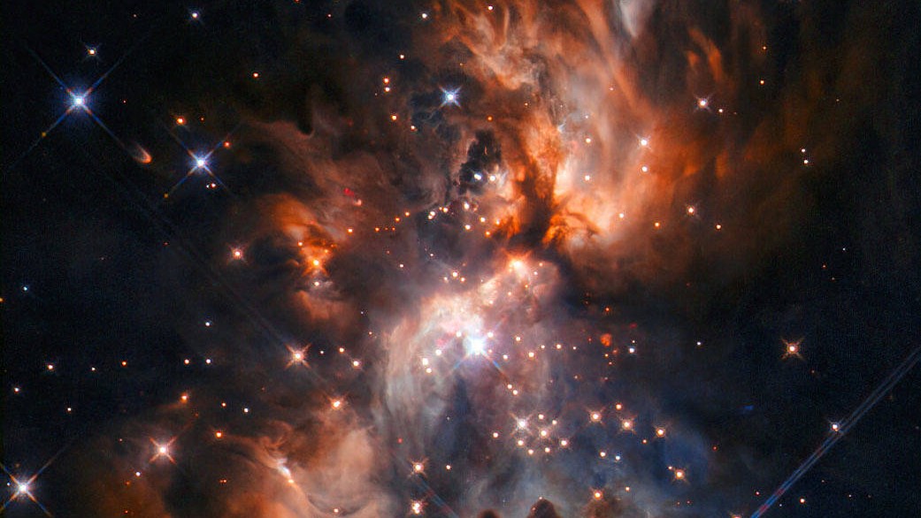 Aninhados entre as vastas nuvens de regiões formadoras de estrelas como esta, encontram-se pistas potenciais sobre a formação do nosso Sistema Solar. Esta imagem, feita pelo Telescópio Espacial Hubble, mostra AFGL 5180, um lindo berçário estelar localizado na Constelação de Gêmeos. No centro da imagem, uma estrela massiva está se formando e abrindo cavidades nas nuvens com um par de jatos poderosos, estendendo-se para o canto superior direito e o canto inferior esquerdo da imagem. As estrelas nascem em ambientes empoeirados e, embora essa poeira produza imagens espetaculares, ela muitas vezes dificulta a visão de estrelas incrustadas nela