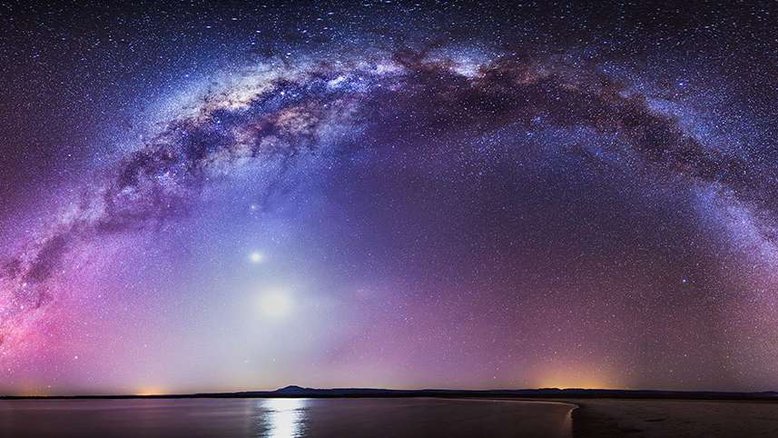 Existe uma estrada que liga a “Cruz do Norte”, apelido dado à boreal Constelação do Cisne, à austral Constelação do Cruzeiro do Sul, mas é preciso estar no local e na hora certa para a ver. A estrada, conforme retratado nesta imagem, é a faixa central da Via Láctea, registrada nesta foto realizada, em outubro de 2018, em Laguna Cejar, no Salar de Atacama, Chile. A Lua brilha abaixo do arco de nossa galáxia, tendo o planeta Vênus logo acima. Saturno e Mercúrio também cintilam pouco abaixo do nosso satélite natural