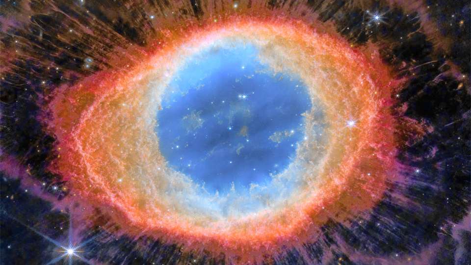 A Nebulosa do Anel (M57) é mais complexa do que parece à primeira vista. Seu anel central tem cerca de um ano-luz de diâmetro, mas esta notável exposição do Telescópio Espacial James Webb explora esta popular nebulosa com uma exposição profunda em luz infravermelha. M57 é uma nebulosa planetária alongada, um tipo de nuvem de gás criada quando uma estrela semelhante ao Sol evolui para se livrar de sua atmosfera externa e se tornar uma estrela anã branca. O oval central da Nebulosa do Anel fica a cerca de 2,5 anos-luz de distância, na direção da Constelação da Lira