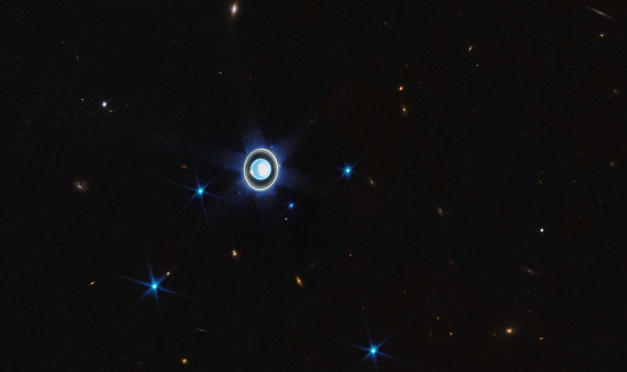 Em abril deste ano, o Telescópio Espacial James Webb obteve imagens impressionantes do planeta Urano. Sétimo planeta a partir do Sol, Urano é singular: ele gira de lado, em um ângulo de aproximadamente 90 graus em relação ao plano de sua órbita. Isto provoca estações climáticas extremas, uma vez que os pólos do planeta experimentam muitos anos de luz solar constante, seguidos por um número igual de anos de escuridão completa. Urano tem 13 anéis conhecidos e 11 deles estão visíveis na imagem, assim como muitas de suas 27 luas conhecidas